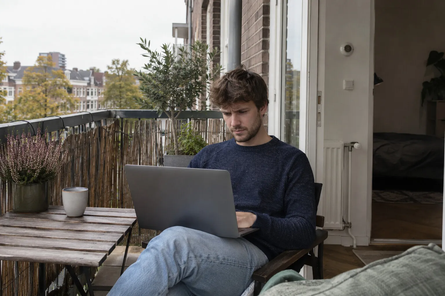 Jonge man op het balkon van een flat bekijkt een mail op zijn laptop