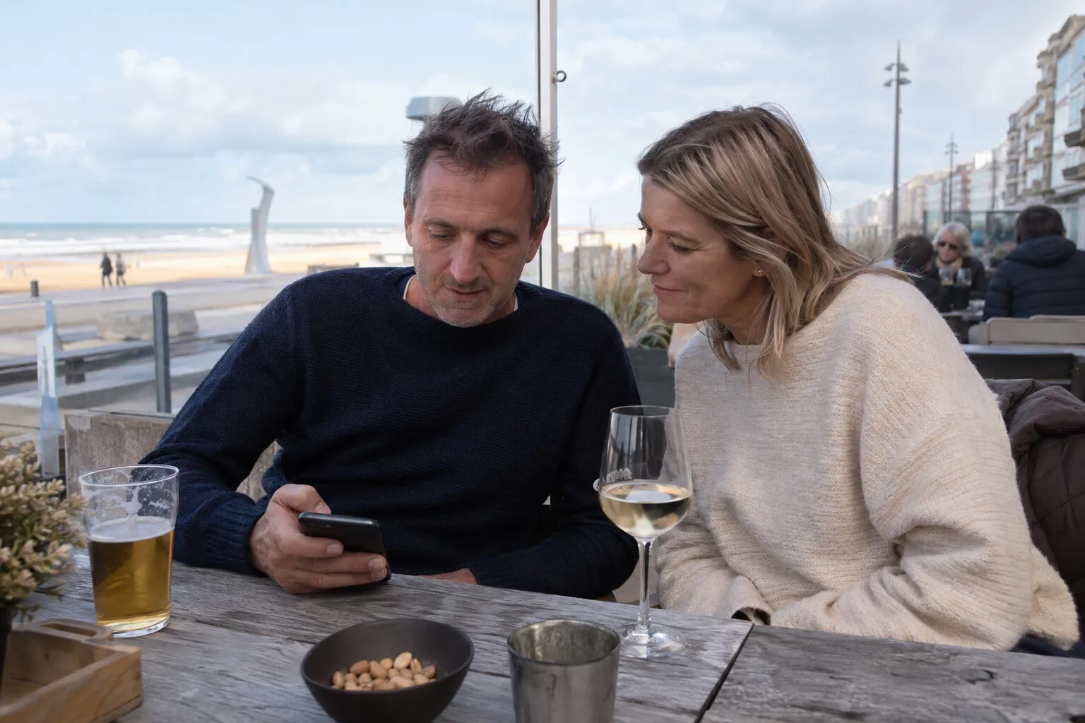 Koppel op een hotelterras aan de kust leest samen een WhatsApp-bericht